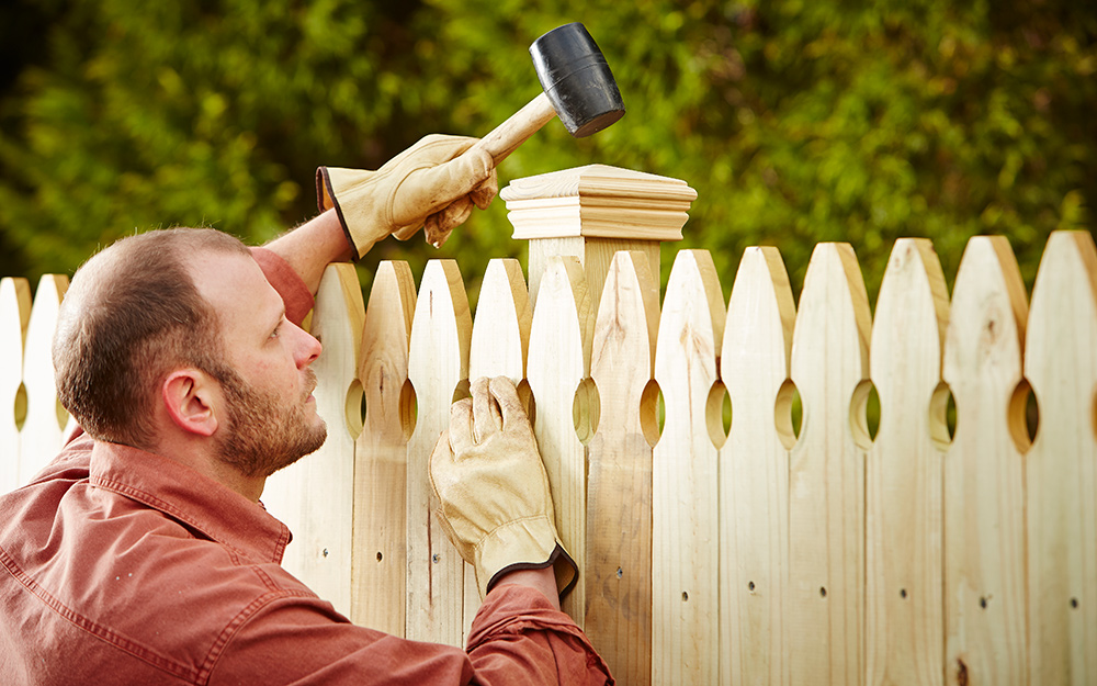 A person uses a mallet to a attach a post cap to a fence.