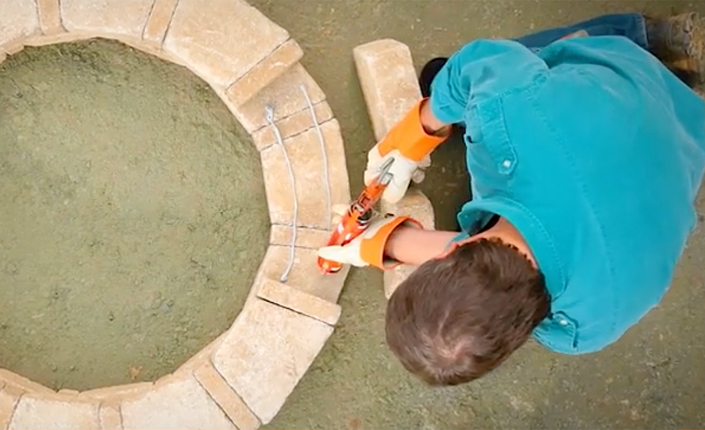 A person applying construction adhesive to pavers for a fire pit.