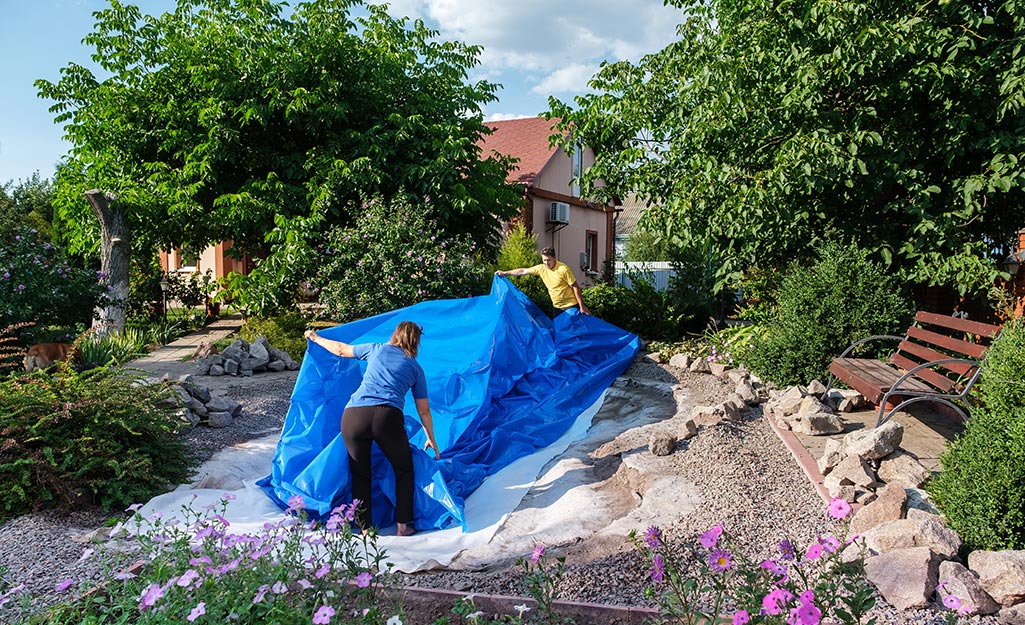 Two people laying a pond liner as they build an in-ground fish pond.