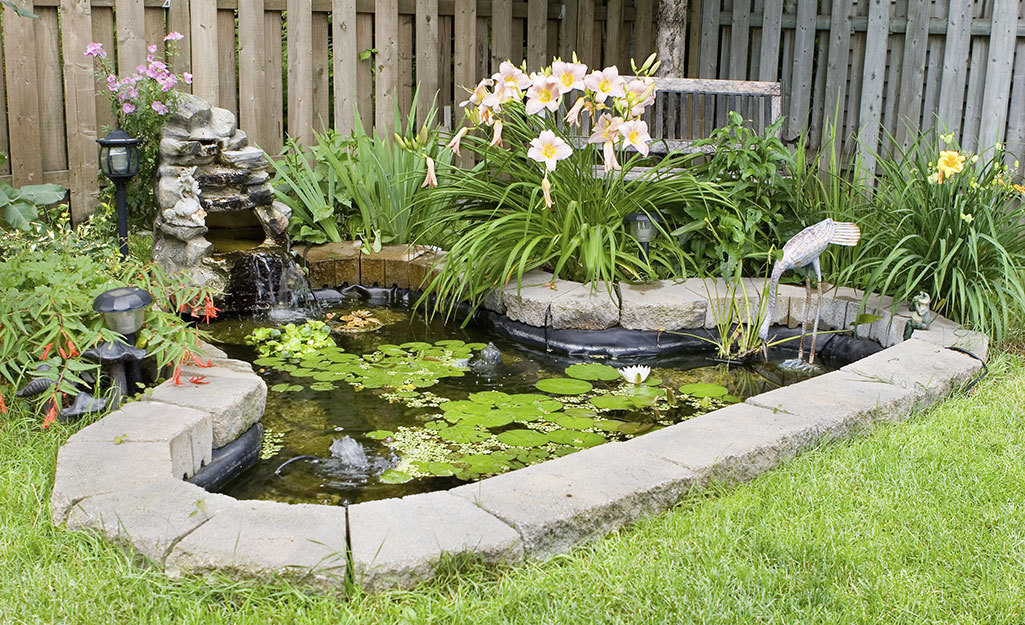 A small pond brims with floating lily pads and is surrounded by a daylilies and a waterfall.