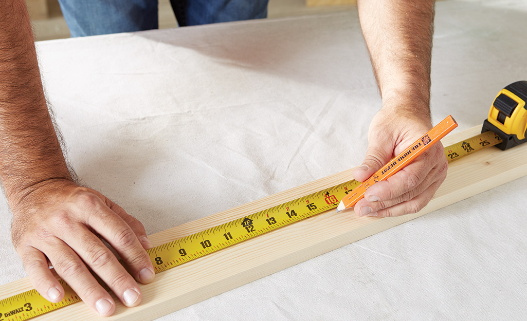 A man uses a pencil and measuring tape to measure and mark wood.