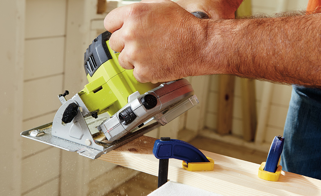 A person uses a circular saw to cut wood. 