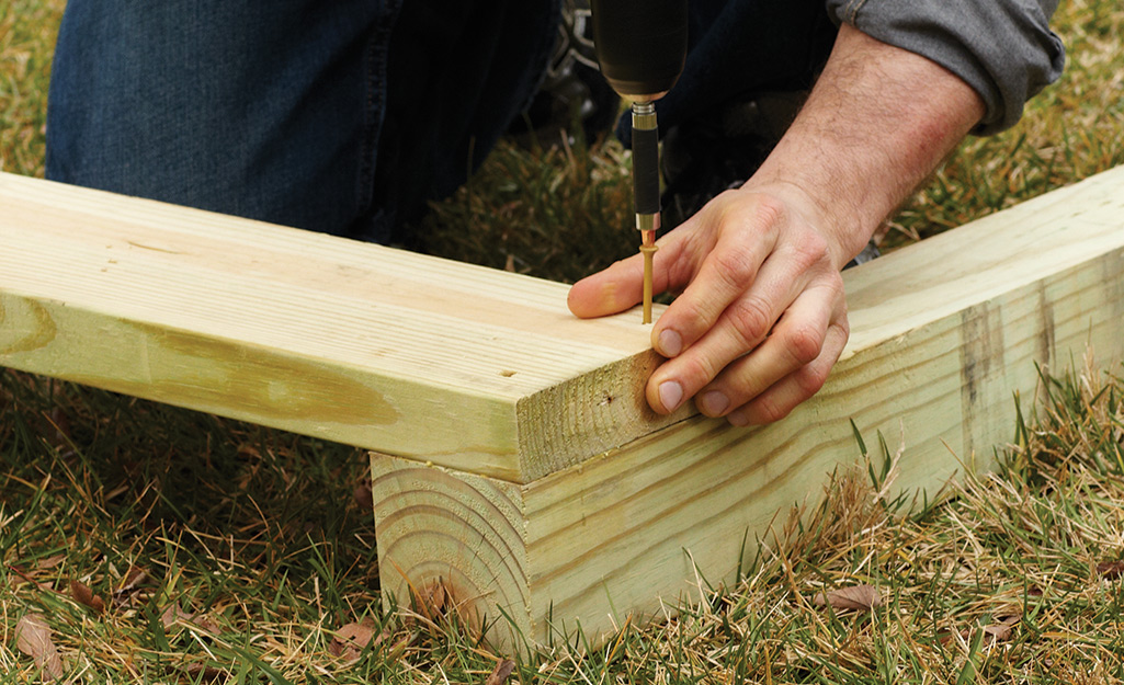 A worker drills together two pieces of lumber for the side wall frame.