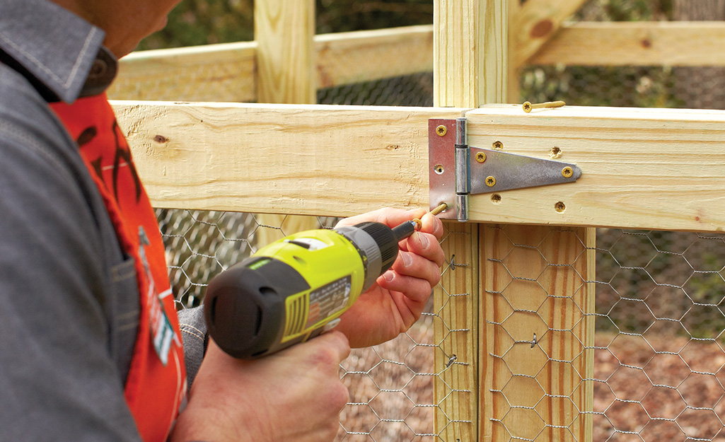 A worker drills in hingers to complete the door of the enclosure.