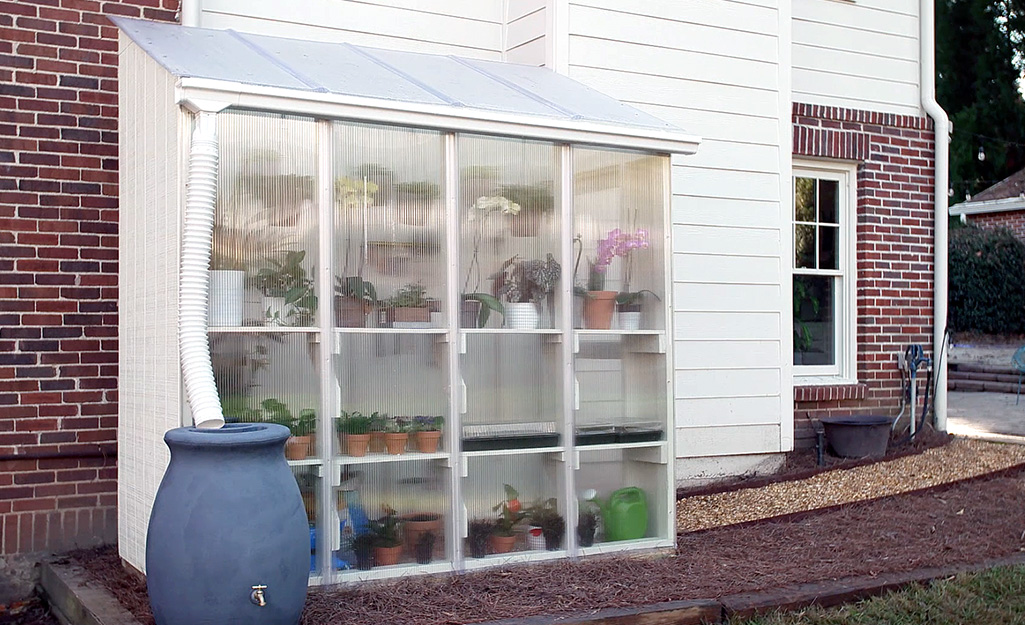 A greenhouse stands adjacent to the back of a brick house.