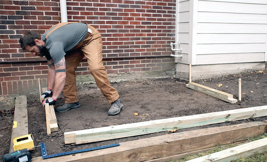 A man places pieces of wood to serve as the base for a greenhouse under construction.