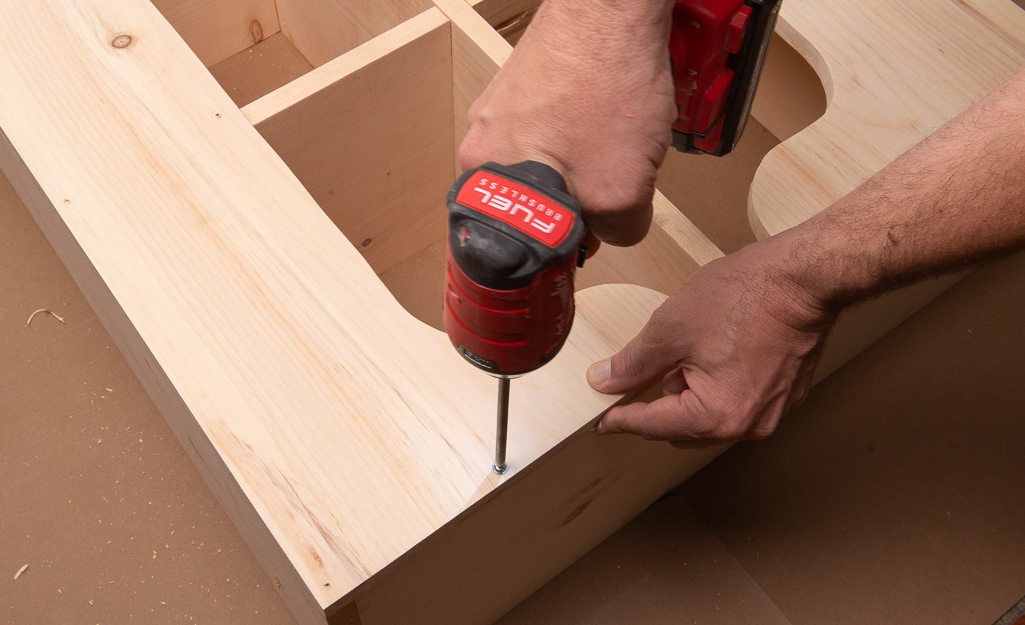 A person drilling screws into the backing of the cubby storage.