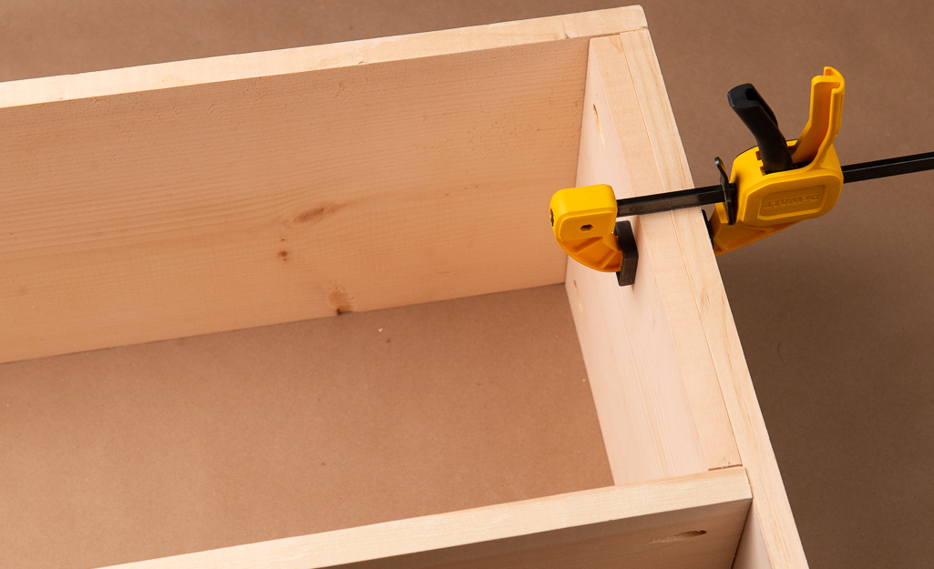 A clamp holding glued boards in place on a cubby.