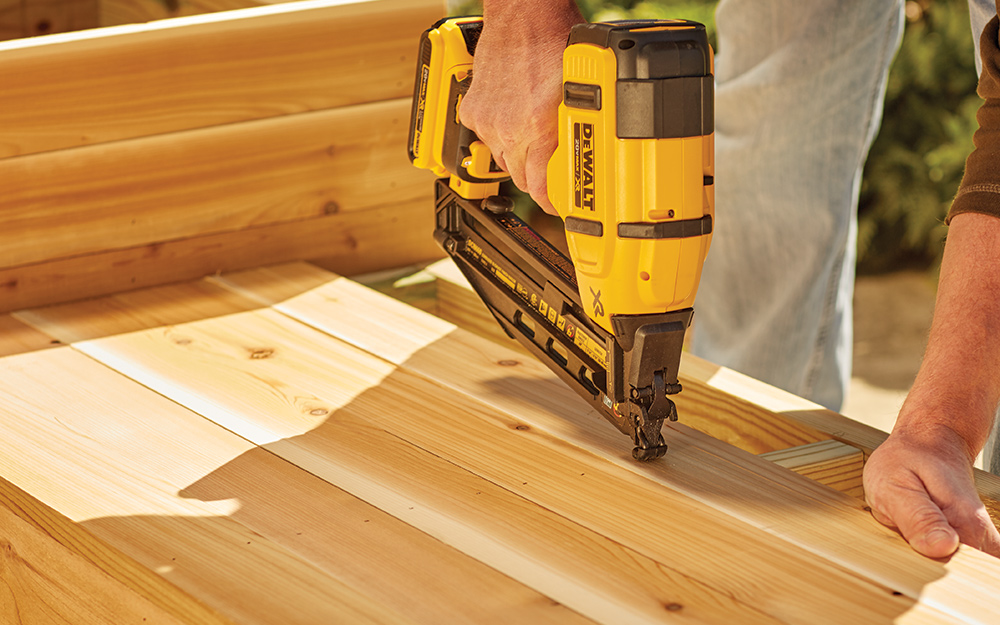 person applying finishing nails to a wooden frame person applying finishing nails to a wooden frame