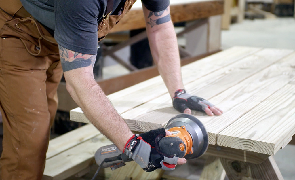 Someone sanding a wood picnic table.