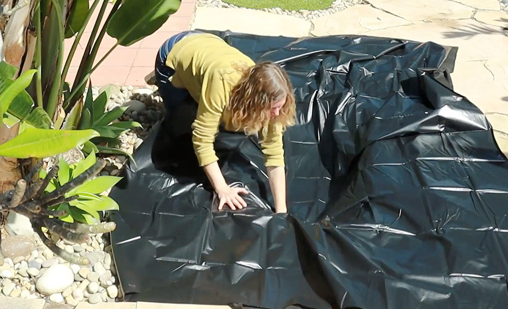 A woman reaches into the center of a piece of pond liner as she places it in a hole for a small pond.