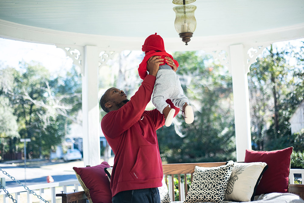 A person holding up a young child on the front porch