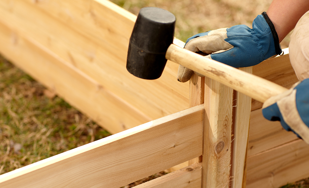 A person using a rubber mallet to build a raised garden bed.