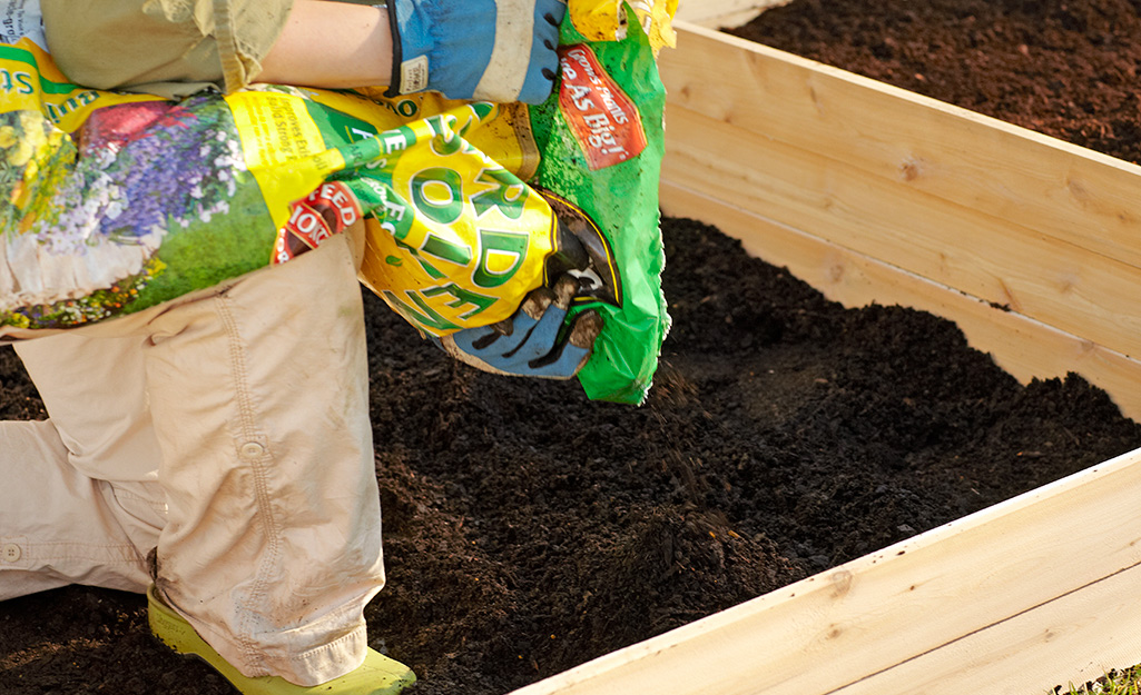 A person adding soil to a raised garden bed.