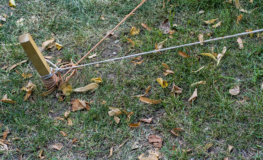 A garden stake and string marking a building location in a yard.
