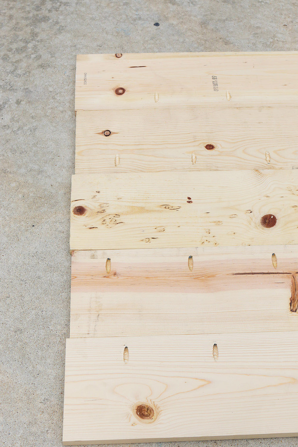 A group of lumber laid out on concrete with pocket holes.