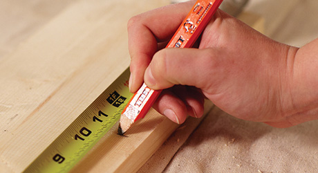 A person measuring a wood board and marking it with a pencil.