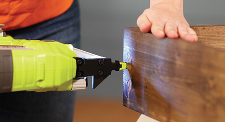 A person using a nail gun to nail the corner of a wood box.