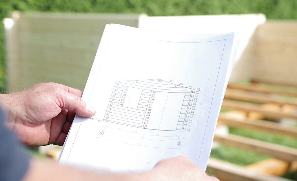 A person holds blueprints for how to build a shed.