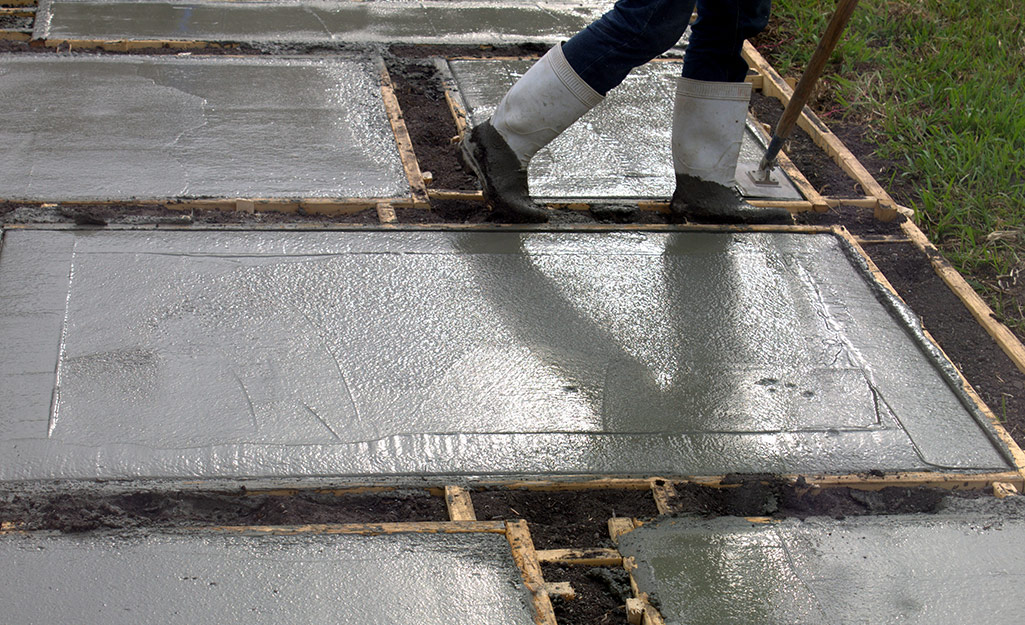 A person standing near freshly poured concrete for the shed foundation.