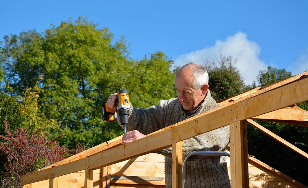A man drilling into the post for the roof of a shed.