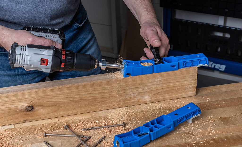 A person uses a drill and a pocket hole jig to drill pocket holes in a piece of wood.