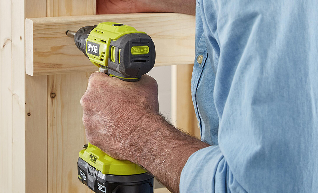 A person uses a drill to attach a fastener to a piece of wood.