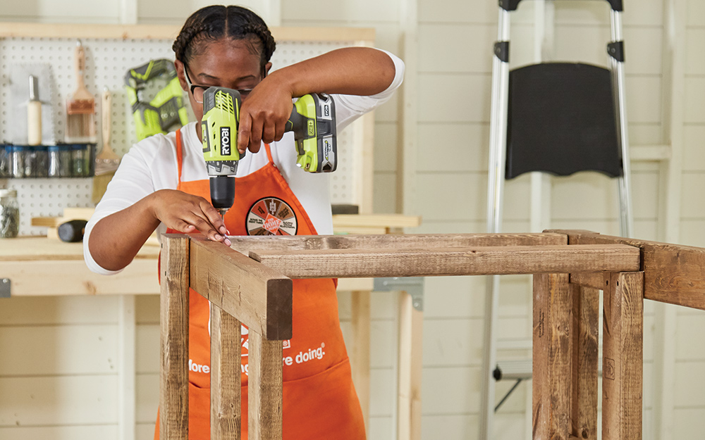 Woman attaches sides together with drill and screws. Woman attaches sides together with drill and screws.