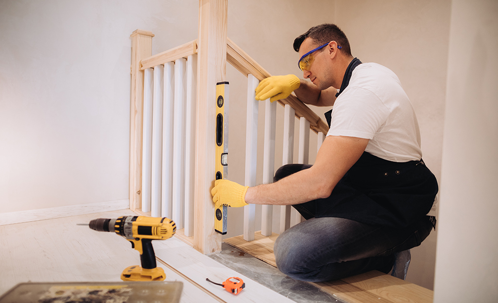A man wearing safety glasses and gloves kneels to use a level at the top of a DIY staircase. A man wearing safety glasses and gloves kneels to use a level at the top of a DIY staircase.