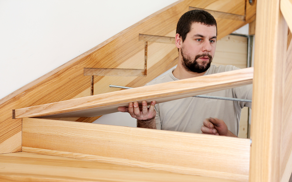 A man puts a tread in place as he builds a staircase.