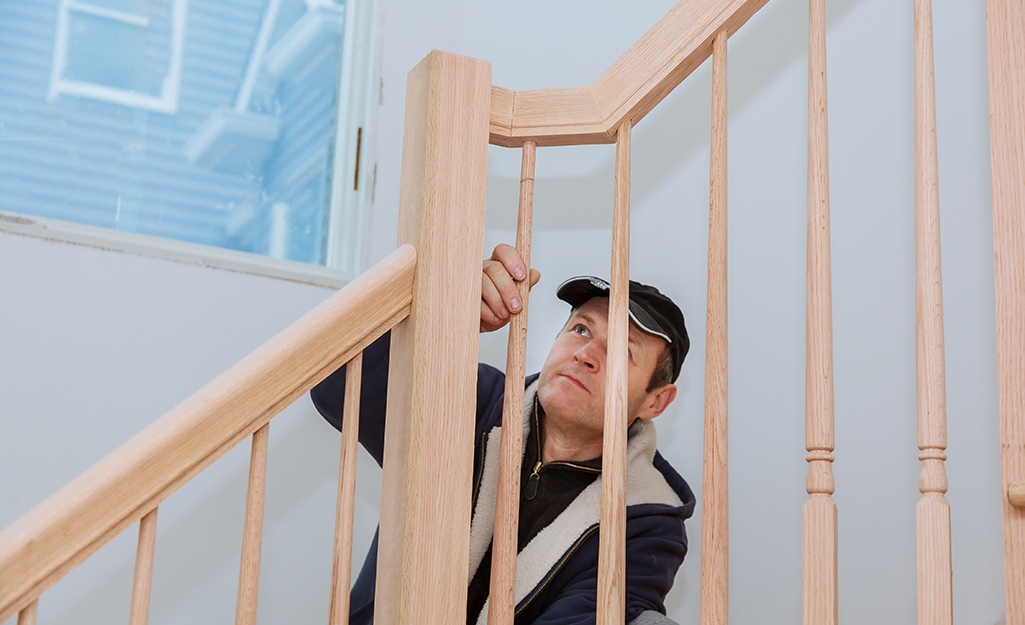 A man adjusts one of the wood balusters below the handrail of a staircase.