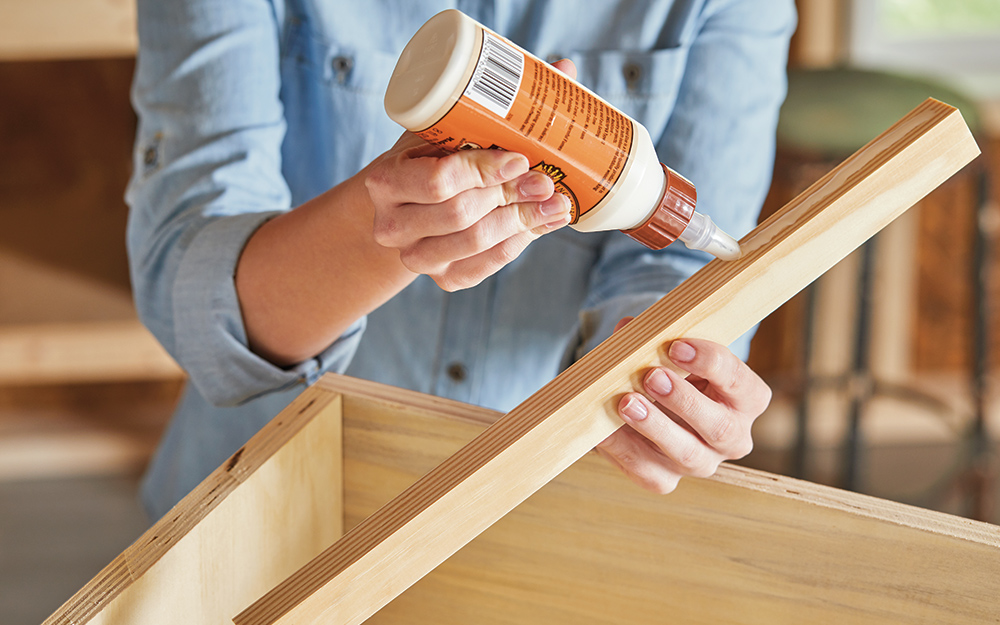 A person applies wood glue to one of the corner braces.