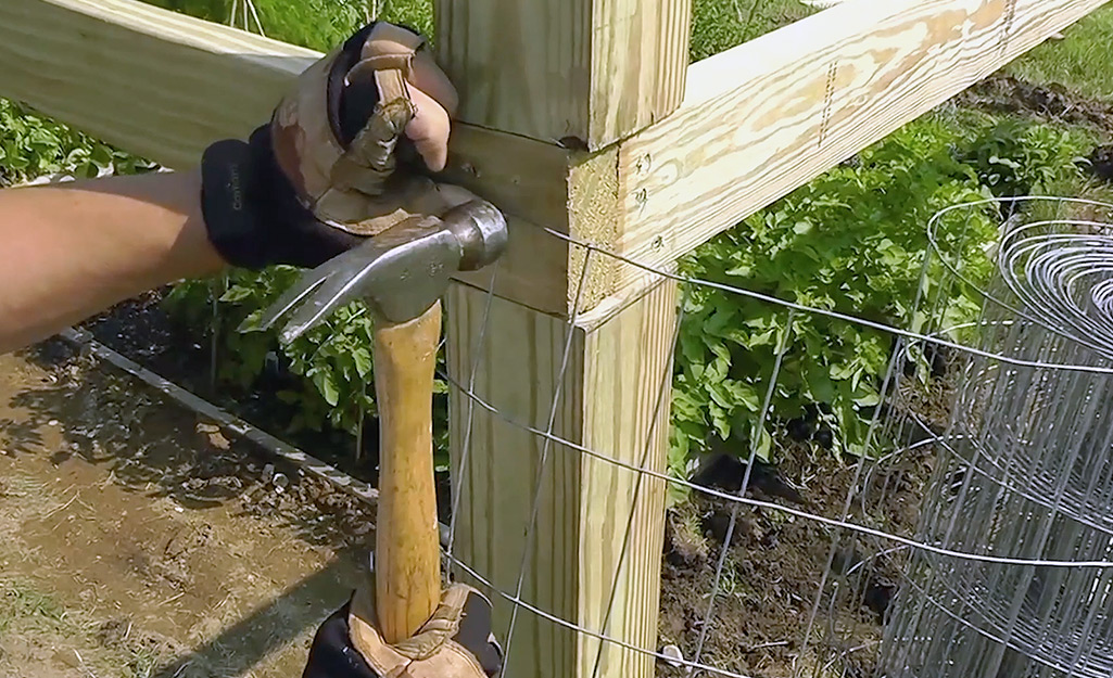 A person nailing a new roll of wire mesh onto a fence post.