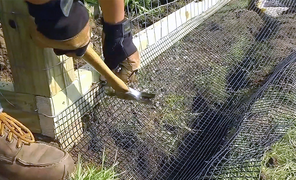A person attaching PVC-coated wire mesh to the bottom of a wire fence.