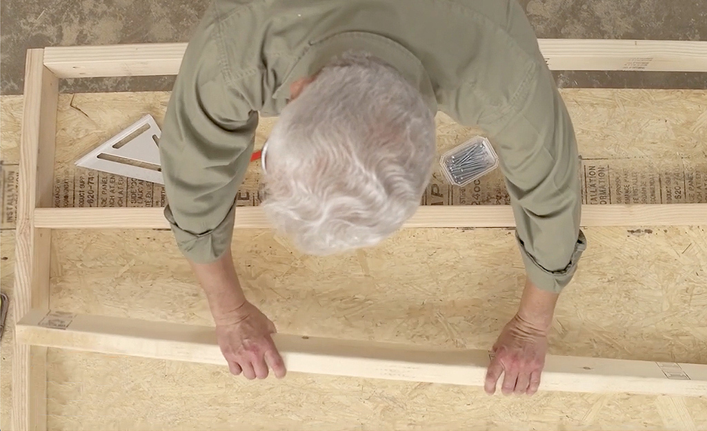 A man adds center supports to the middle of the wooden bed frame’s cross braces