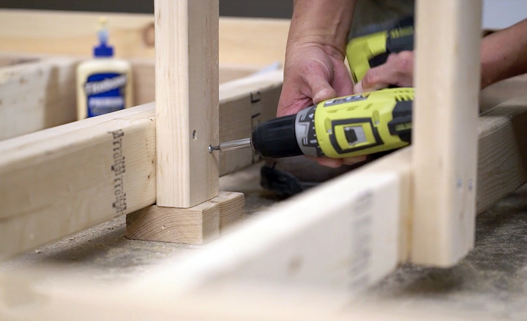 A man drills two pieces of lumber together. A man drills two pieces of lumber together.