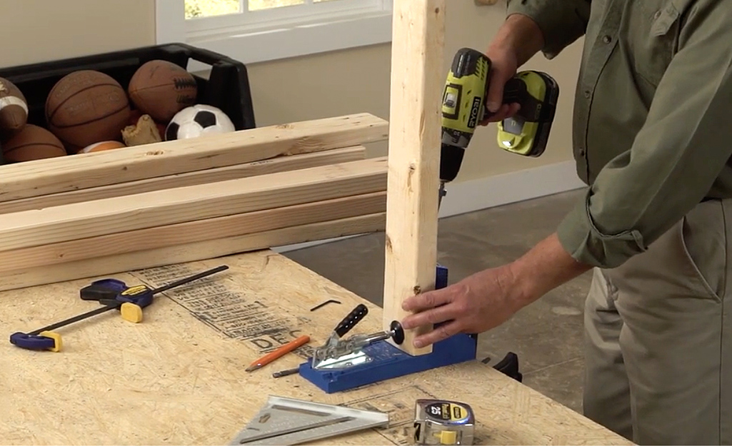 A man uses a jig to create pocket holes in the pieces of the wooden bed frame A man uses a jig to create pocket holes in the pieces of the wooden bed frame