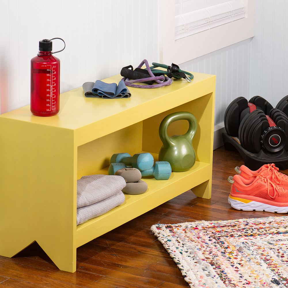 A wooden storage bench painted yellow holding workout gear.