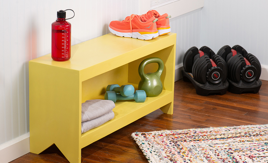 A wooden storage bench painted yellow with workout gear on it.