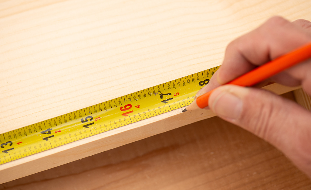 A person measuring and marking a board.