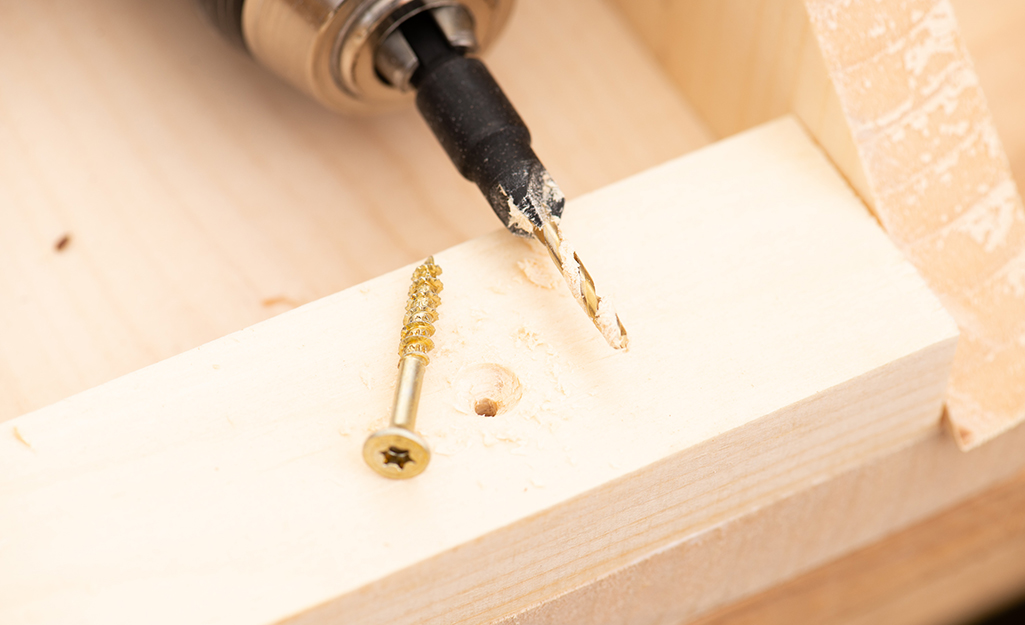 A drill bit and screw on a wooden board with a pilot hole.