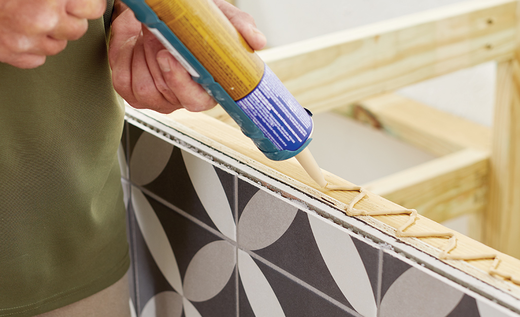 A person adds glue to the top of a DIY outdoor kitchen counter frame.