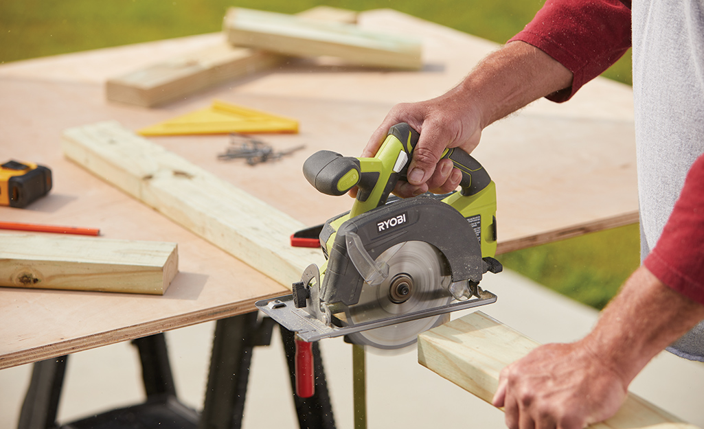 A person saws wood boards for an outdoor kitchen.