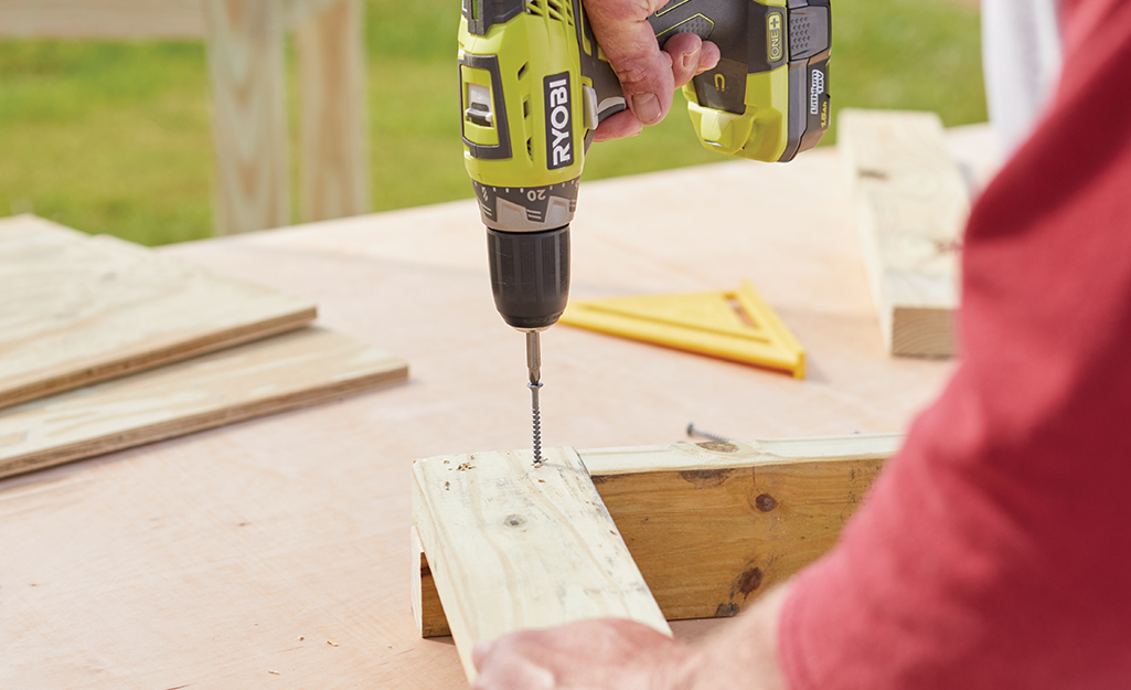 A person fastens a two pressure-treated boards with screws.