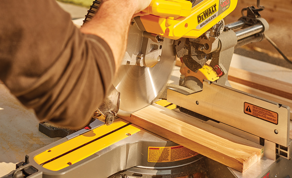 A person using a power miter saw cutting into a piece of lumber