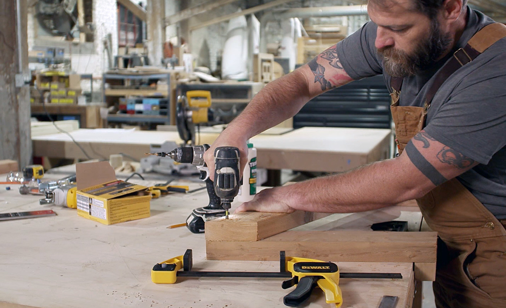 A man uses a drill to connect one piece of wood to another. A man uses a drill to connect one piece of wood to another.