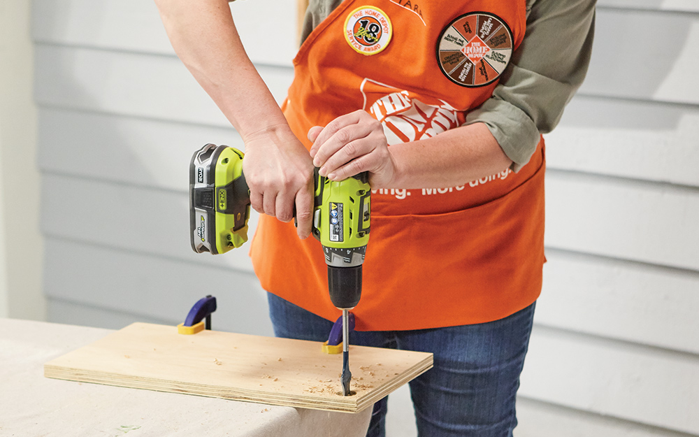A Home Depot Associate drills holes into a board for a DIY crate end table. A Home Depot Associate drills holes into a board for a DIY crate end table.