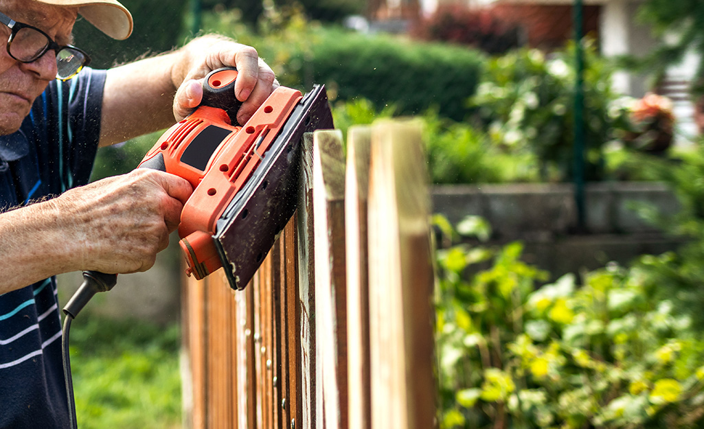 A person shaping a fence picket with a sander.
