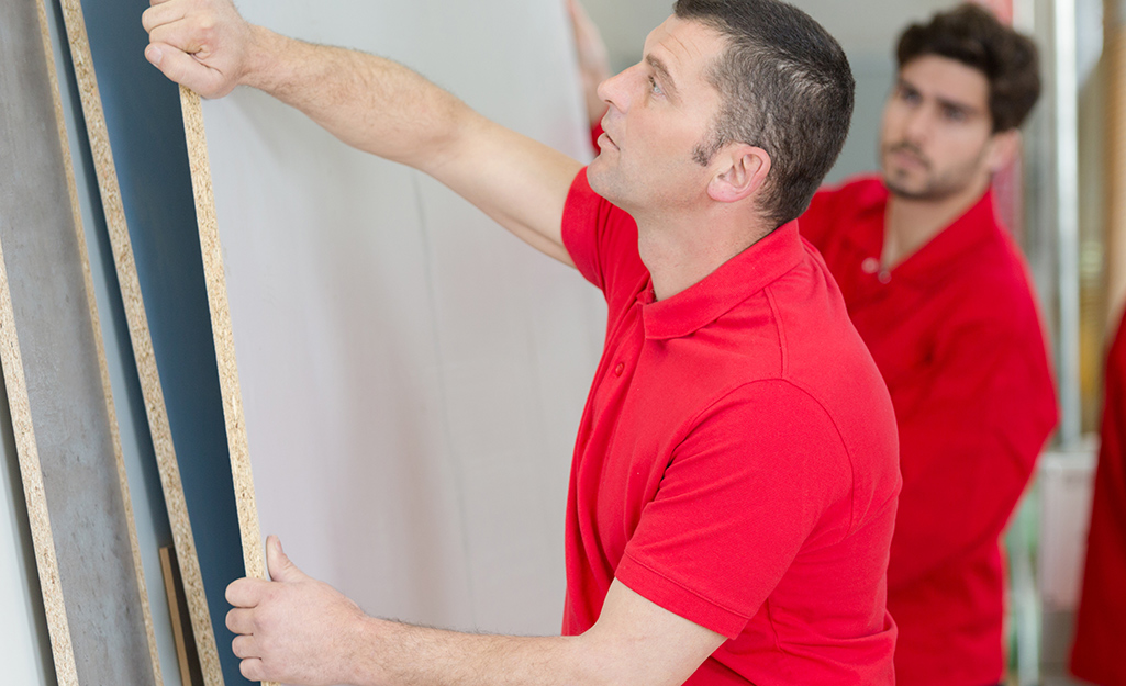 Two men positioning pieces of plywood against a wall. Two men positioning pieces of plywood against a wall.