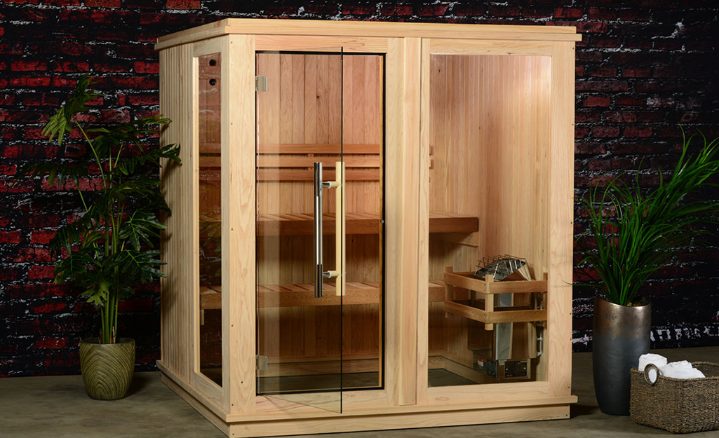 Two benches inside of a large wood home sauna can be seen through its open glass door and front glass wall.